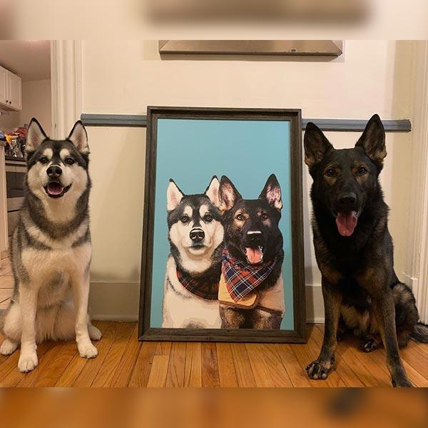 Two real dogs sitting on either side of a framed portrait of two dogs in a kitchen.